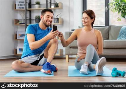 fitness, sport and technology concept - happy couple with smartphone doing sports at home. happy couple with smartphone doing sports at home