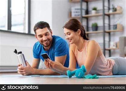 fitness, sport and technology concept - happy couple with smartphone having break at home. happy couple with smartphone after sports at home