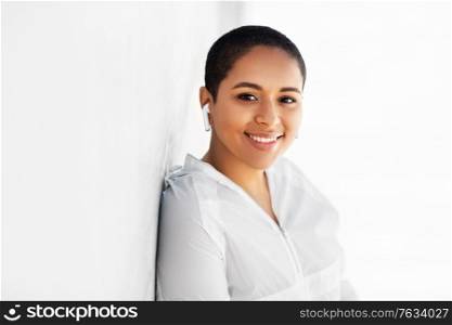 fitness, sport and technology concept - happy smiling young african american woman with wireless earphones listening to music outdoors. happy african american woman with earphones