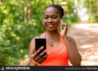 fitness, sport and technology concept - happy smiling young african american woman with earphones listening to music on smartphone outdoors. african american woman with earphones and phone