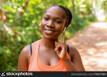 fitness, sport and technology concept - happy smiling young african american woman with wireless earphones listening to music outdoors. happy african american woman with earphones