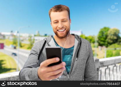 fitness, sport and technology concept - happy smiling young man with earphones and smartphone listening to music outdoors. smiling young man with earphones and smartphone