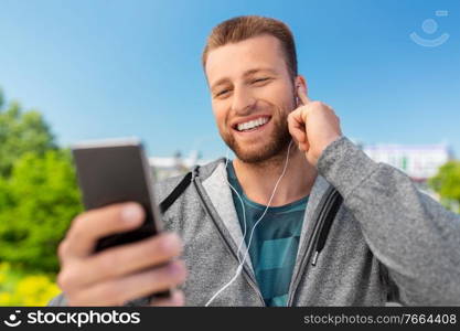 fitness, sport and technology concept - happy smiling young man with earphones and smartphone listening to music outdoors. smiling young man with earphones and smartphone