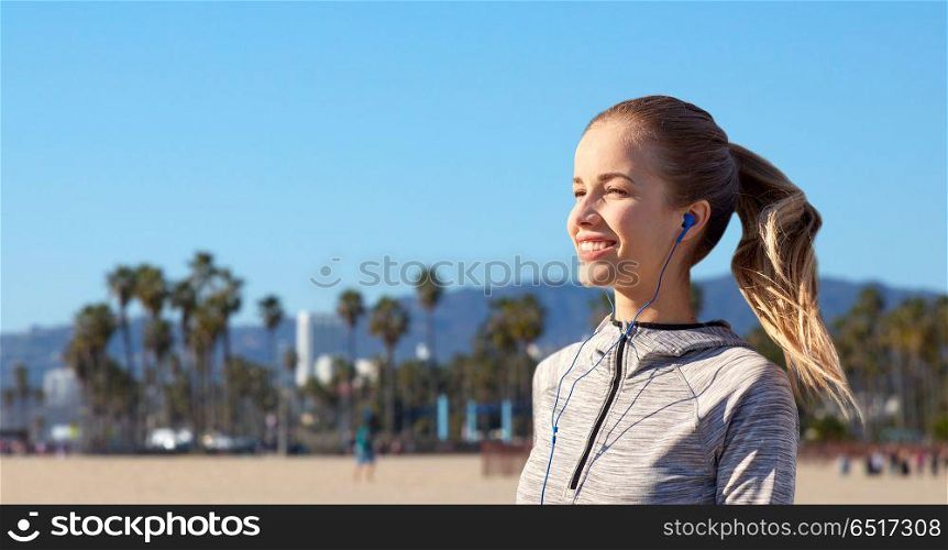 fitness, sport and technology concept - happy woman listening to music in earphones over venice beach background in california. happy woman listening to music in earphones. happy woman listening to music in earphones