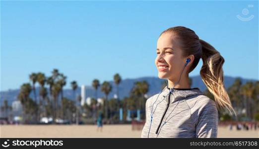 fitness, sport and technology concept - happy woman listening to music in earphones over venice beach background in california. happy woman listening to music in earphones. happy woman listening to music in earphones