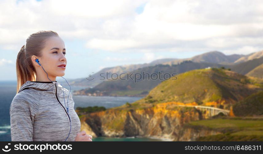 fitness, sport and technology concept - happy woman running and listening to music in earphones over bixby creek bridge on big sur coast of california background. woman with earphones running over big sur coast. woman with earphones running over big sur coast