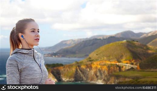 fitness, sport and technology concept - happy woman running and listening to music in earphones over bixby creek bridge on big sur coast of california background. woman with earphones running over big sur coast. woman with earphones running over big sur coast