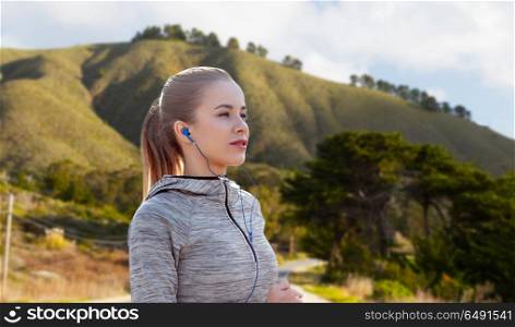 fitness, sport and technology concept - happy woman running and listening to music in earphones over big sur hills background in california. woman with earphones running over big sur hills. woman with earphones running over big sur hills