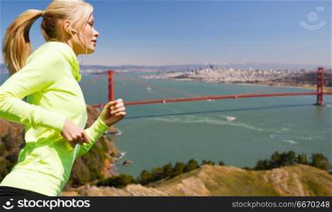 fitness, sport and technology concept - happy woman running and listening to music in earphones over golden gate bridge in san francisco bay background. woman with earphones running over san francisco. woman with earphones running over san francisco