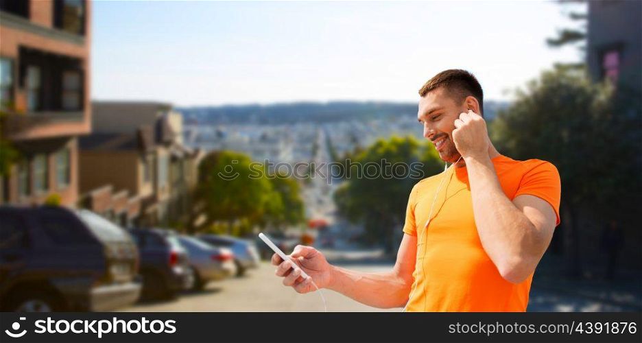 fitness, sport and technology concept - smiling man with smartphone and earphones listening to music over san francisco city background. man with smartphone and earphones in san francisco. man with smartphone and earphones in san francisco