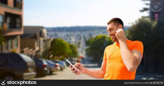 fitness, sport and technology concept - smiling man with smartphone and earphones listening to music over san francisco city background. man with smartphone and earphones in san francisco. man with smartphone and earphones in san francisco