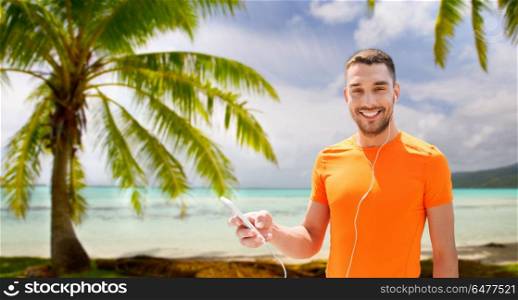 fitness, sport and technology concept - smiling man with smartphone and earphones listening to music over tropical beach background in french polynesia. man with smartphone and earphones over beach. man with smartphone and earphones over beach