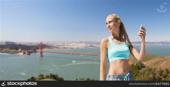 fitness, sport and technology concept - smiling young woman with smartphone exercising over golden gate bridge in san francisco bay background. woman with smartphone doing sports over bridge. woman with smartphone doing sports over bridge