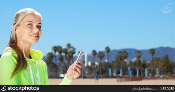 fitness, sport and technology concept - woman with earphones and smartphone listening to music over venice beach background in california. woman listening to music outdoors. woman listening to music outdoors