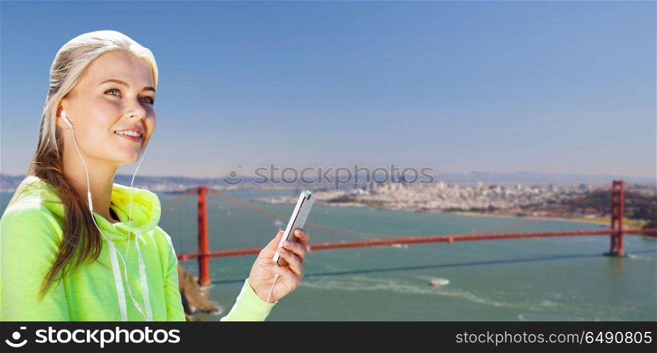 fitness, sport and technology concept - woman with earphones and smartphone listening to music over golden gate bridge in san francisco bay background. sportswoman listening to music over san francisco. sportswoman listening to music over san francisco