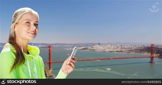 fitness, sport and technology concept - woman with earphones and smartphone listening to music over golden gate bridge in san francisco bay background. sportswoman listening to music over san francisco. sportswoman listening to music over san francisco
