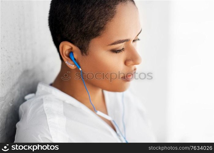 fitness, sport and technology concept - young african american woman with earphones listening to music outdoors. african american woman with earphones