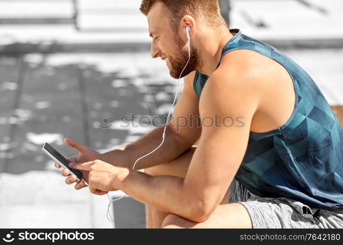 fitness, sport and technology concept - young athlete man with earphones and smartphone listening to music outdoors. young athlete man with earphones and smartphone