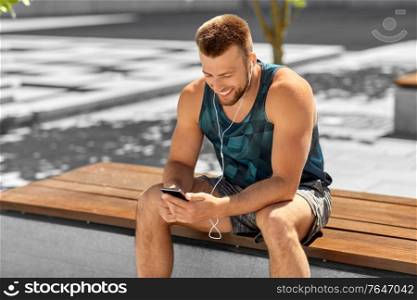 fitness, sport and technology concept - young athlete man with earphones and smartphone listening to music outdoors. young athlete man with earphones and smartphone