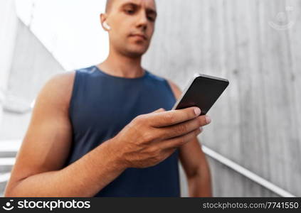 fitness, sport and technology concept - young athlete man with earphones and smartphone listening to music outdoors. young athlete man with earphones and smartphone