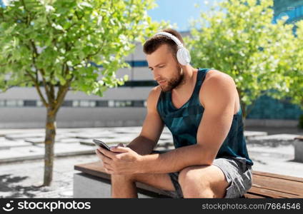 fitness, sport and technology concept - young athlete man with headphones and smartphone listening to music outdoors. young athlete man with headphones and smartphone