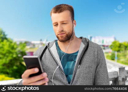 fitness, sport and technology concept - young man with earphones and smartphone listening to music outdoors. young man with earphones and smartphone