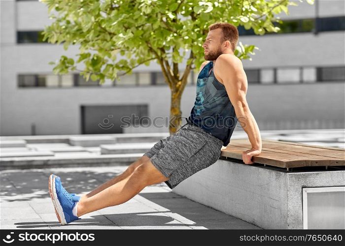 fitness, sport and training concept - young man doing triceps dip on city street. young man doing triceps dip on city street