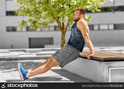 fitness, sport and training concept - young man doing triceps dip on city street. young man doing triceps dip on city street