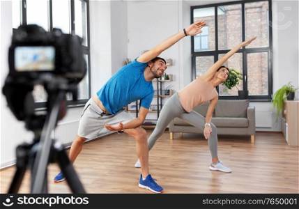 fitness, sport and video blogging concept - couple of bloggers with camera on tripod recording online yoga class at home. couple recording home yoga class video