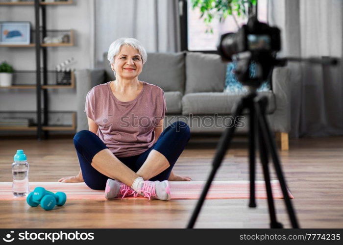 fitness, sport and video blogging concept - happy senior woman or blogger with camera streaming online class at home. woman or fitness blogger with camera at home