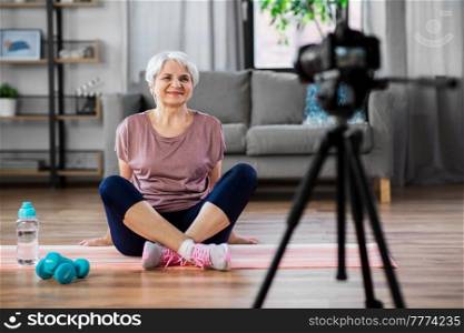 fitness, sport and video blogging concept - happy senior woman or blogger with camera streaming online class at home. woman or fitness blogger with camera at home