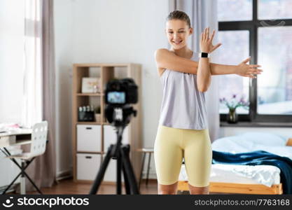 fitness, sport and video blogging concept - happy smiling teenage girl or blogger with camera on tripod recording online class at home. teenage girl or blogger recording gym class video