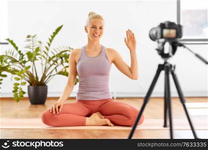 fitness, sport and video blogging concept - happy smiling young woman or blogger with camera on tripod recording online yoga class at home or studio. woman with camera streaming for yoga blog at home