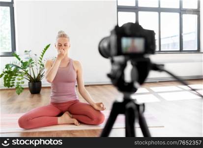 fitness, sport and video blogging concept - woman or blogger with camera on tripod recording online yoga class in gym or studio. woman or blogger recording gym yoga class video