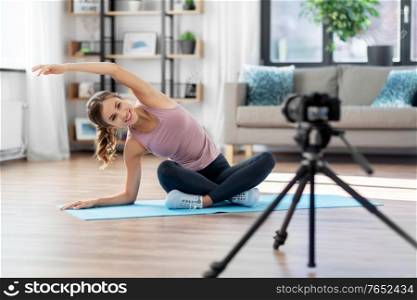 fitness, sport and video blogging concept - woman or blogger with camera streaming online yoga class at home. woman or sports blogger streaming online yoga