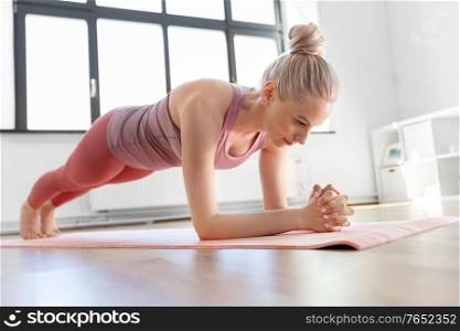 fitness, sport and yoga concept - young woman doing plank exercise on mat at home. young woman doing plank exercise on mat at home