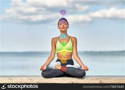 fitness, sport and yoga concept - young woman meditating in lotus pose at seaside with seven chakra symbols. woman meditating in lotus pose with seven chakras