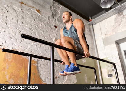 fitness, sport, bodybuilding and people concept - young man doing abdominal exercise on parallel bars in gym. man flexing abs on parallel bars in gym