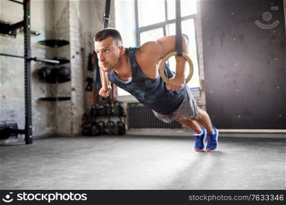 fitness, sport, bodybuilding and people concept - young man doing push-ups on gymnastic rings in gym. man doing push-ups on gymnastic rings in gym