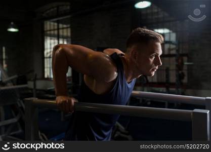 fitness, sport, bodybuilding and people concept - young man doing triceps dip exercise on parallel bars in gym. man doing triceps dip on parallel bars in gym