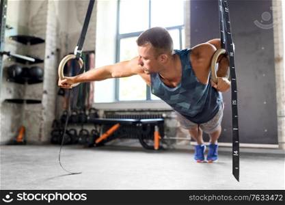 fitness, sport, bodybuilding and people concept - young man exercising on gymnastic rings in gym. man doing exercising on gymnastic rings in gym