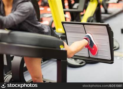 fitness, sport, bodybuilding, exercising and people concept - close up of young woman flexing muscles on leg press machine in gym