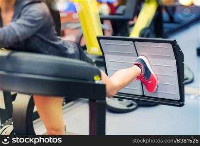 fitness, sport, bodybuilding, exercising and people concept - close up of young woman flexing muscles on leg press machine in gym. woman flexing muscles on leg press machine in gym