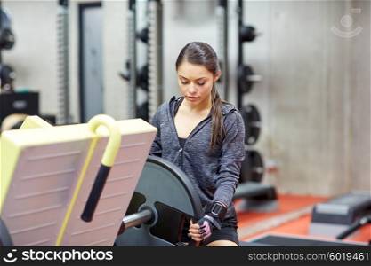 fitness, sport, bodybuilding, exercising and people concept - young woman adjusting leg press machine in gym
