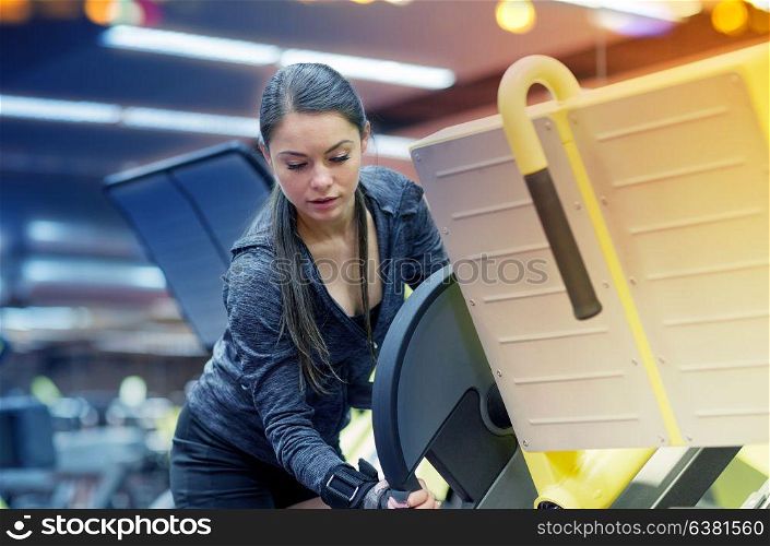 fitness, sport, bodybuilding, exercising and people concept - young woman adjusting leg press machine in gym. young woman adjusting leg press machine in gym