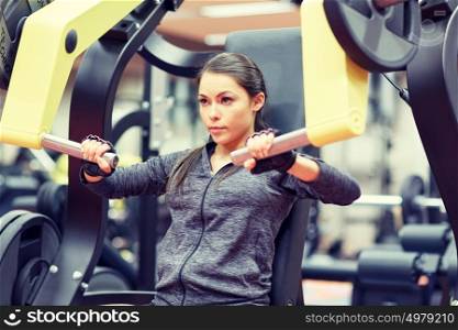 fitness, sport, bodybuilding, exercising and people concept - young woman flexing muscles on seated chest press machine in gym. woman flexing muscles on chest press gym machine