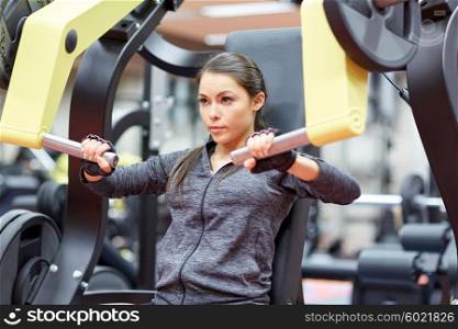 fitness, sport, bodybuilding, exercising and people concept - young woman flexing muscles on seated chest press machine in gym
