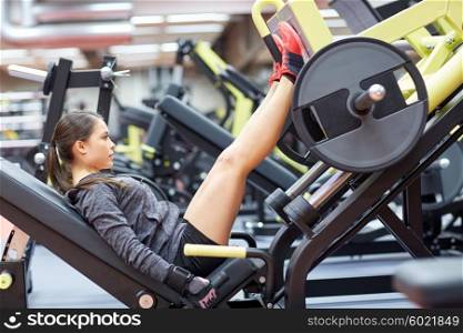 fitness, sport, bodybuilding, exercising and people concept - young woman flexing muscles on leg press machine in gym
