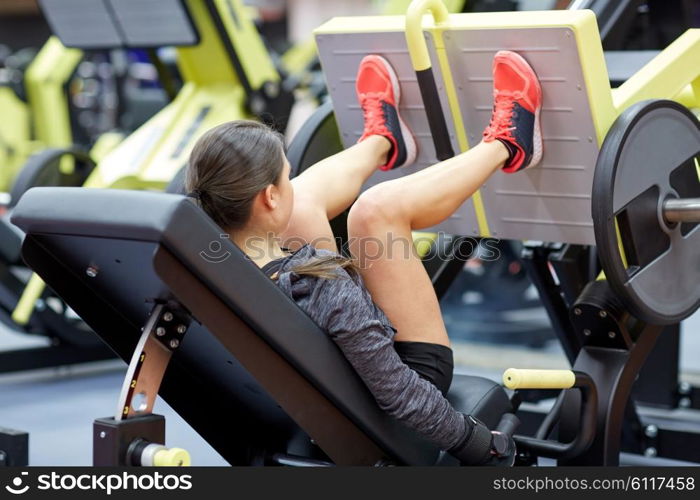 fitness, sport, bodybuilding, exercising and people concept - young woman flexing muscles on leg press machine in gym