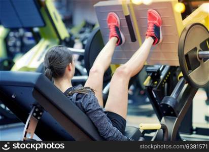 fitness, sport, bodybuilding, exercising and people concept - young woman flexing muscles on leg press machine in gym. woman flexing muscles on leg press machine in gym